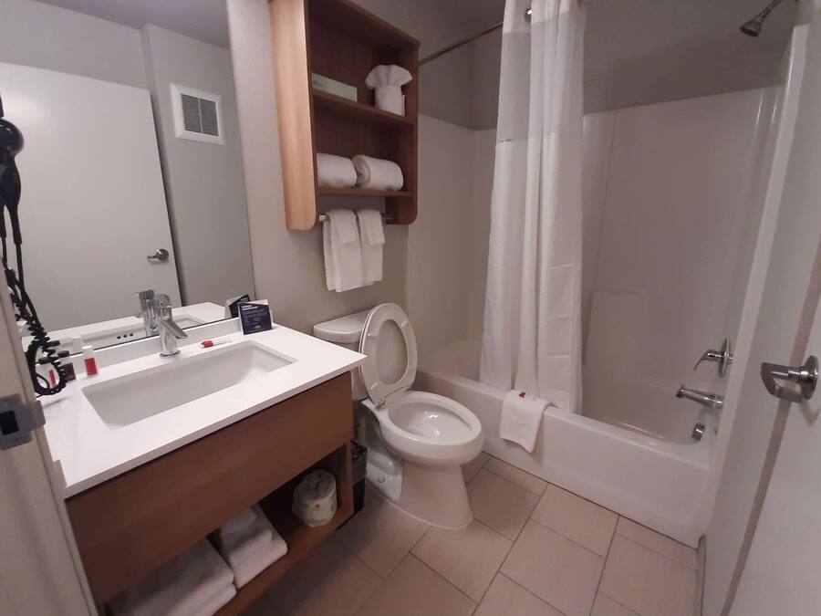 A bathroom with a sink, toilet, and shower. There is a towel rack above the toilet and a shelf with towels.