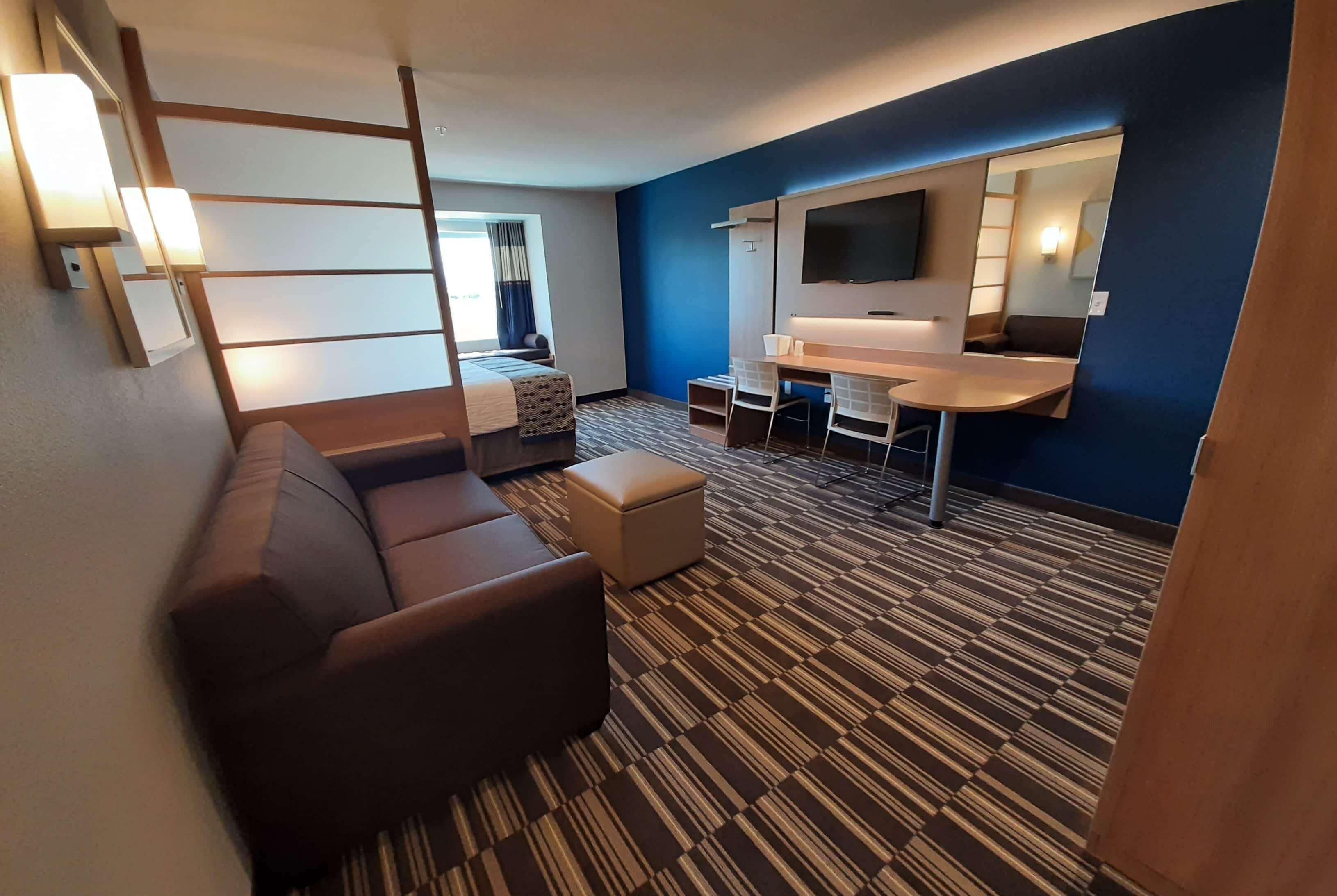 A hotel room with a sofa, a small table, a TV, and a patterned carpet.