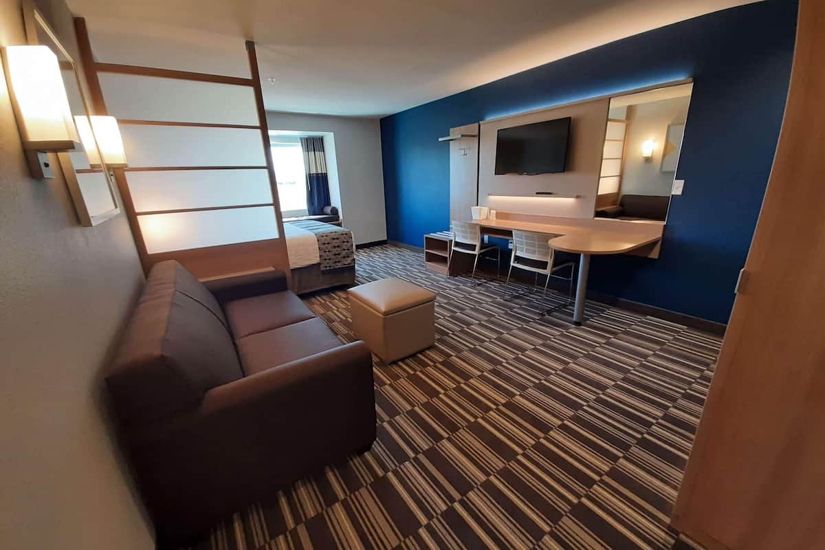 A hotel room with a sofa, a small table, a TV, and a patterned carpet.