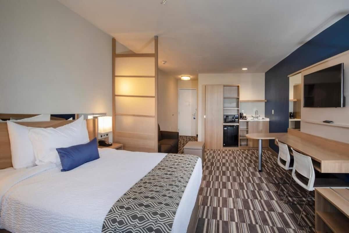 A hotel room with a bed, bedside table, lamp, desk, chair, and a TV mounted on the wall.