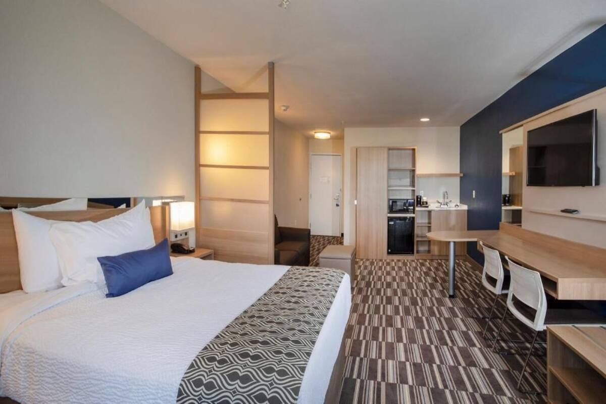A hotel room with a bed, bedside table, lamp, desk, chair, and a TV mounted on the wall.
