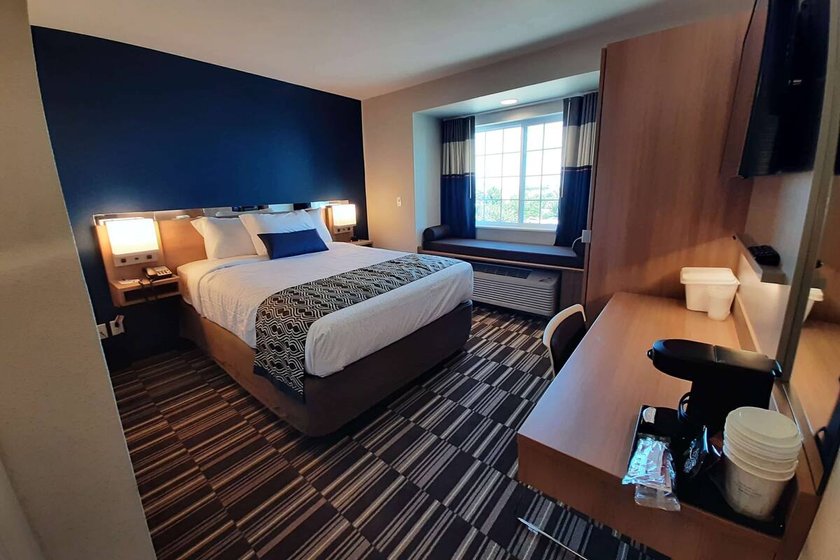 A hotel room with a bed, bedside table, desk, and a window with curtains.