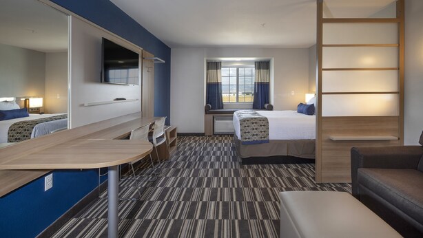 Ein Hotelzimmer mit einem Bett, einem Schreibtisch, einem Sessel, einer Couch, einem Fernseher und einem Fenster mit Vorhängen.