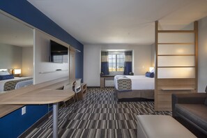 A hotel room with a bed, a desk, a chair, a couch, a TV, and a window with curtains. - Microtel Inn & Suites by Wyndham Loveland (Loveland)
