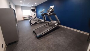 Ein Fitnessraum mit Laufband, Ergometer und einem großen Kühlschrank.