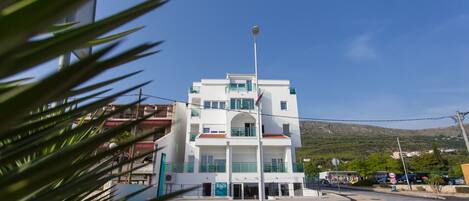 A multi-story building with a central entrance, a flagpole, and a clear view of the surrounding area including a road and distant hills.
