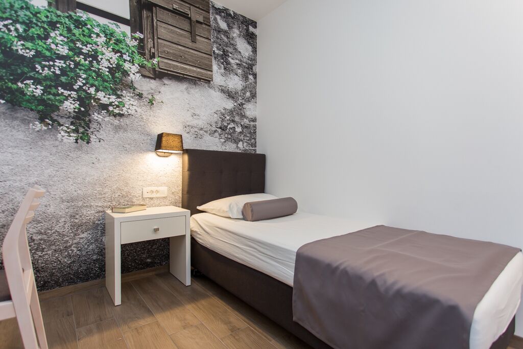 Une chambre à coucher avec un lit, une table de chevet et une étagère fixée au mur, sur laquelle est posée une plante.