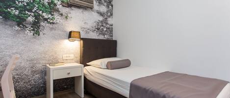 Une chambre à coucher avec un lit, une table de chevet et une étagère fixée au mur, sur laquelle est posée une plante.