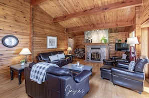 A log cabin interior with a fireplace, leather sofas, a clock, and a framed picture on the wall.
