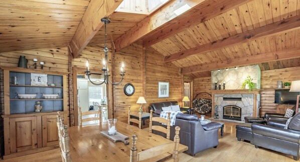 A cozy log cabin interior with a dining area, living room, fireplace, and wooden ceiling beams. - Renovated 4 Bed, 3 Bath. Mins from Port Sandfield. Tennis! Beach! (Minett)