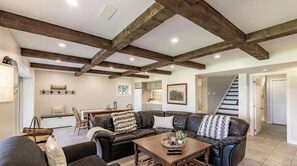 A spacious living area with exposed wooden beams, a black leather sofa, a wooden coffee table, and a kitchen in the background. - Renovated 4 Bed, 3 Bath. Mins from Port Sandfield. Tennis! Beach! (Minett)