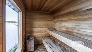 A sauna with wooden walls and benches, a herringbone-patterned floor, and a window overlooking a body of water. - Gorgeous New Build on Rosseau with Pictuesque Views!! Sunset Deck! Sleeps 12! (Seguin)