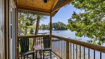 A wooden deck with two chairs and a table, overlooking a lake with trees and a dock.