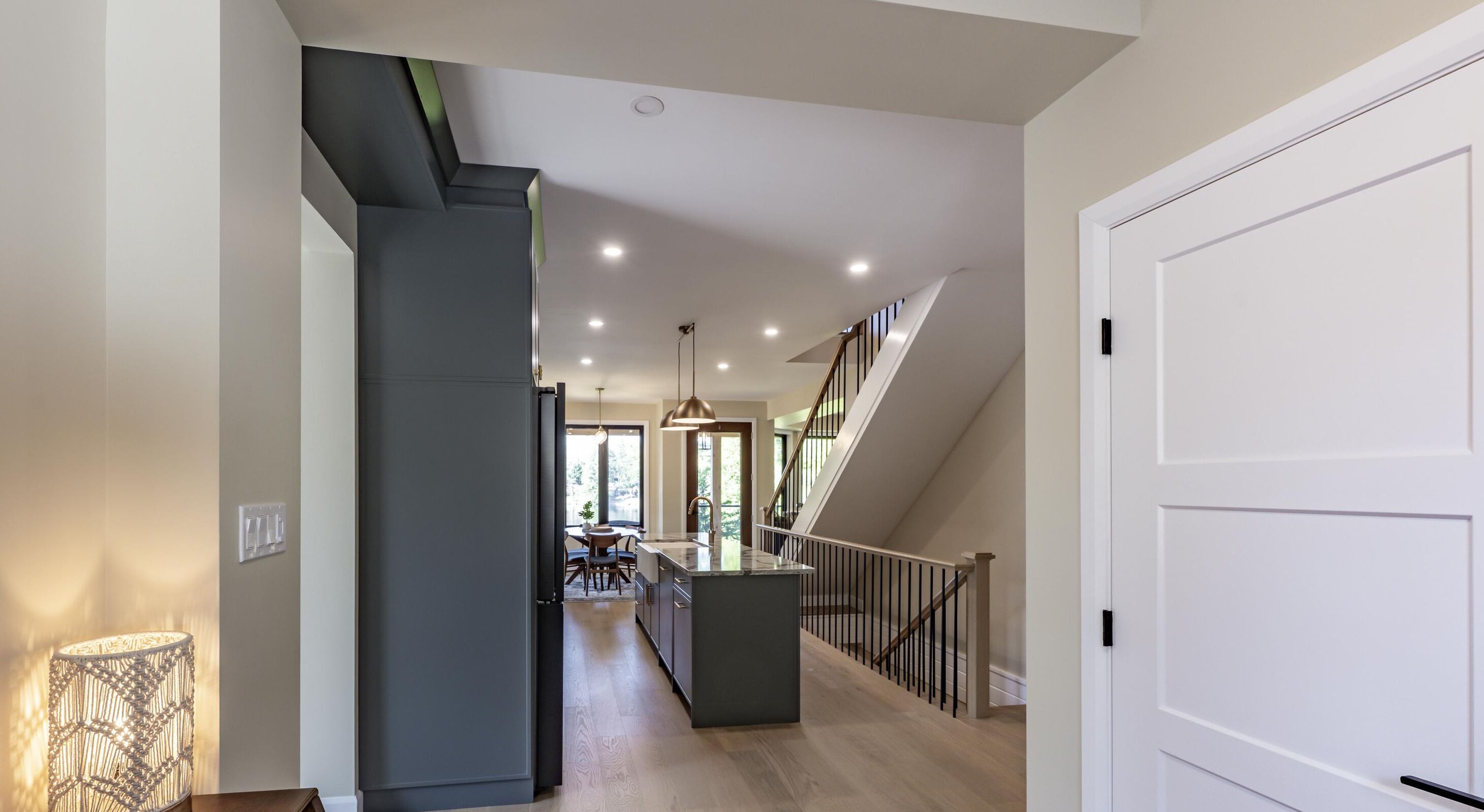 A modern kitchen with a central island, a staircase leading to an upper level, and a dining area visible through an open door.