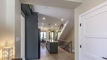 A modern kitchen with a central island, a staircase leading to an upper level, and a dining area visible through an open door.