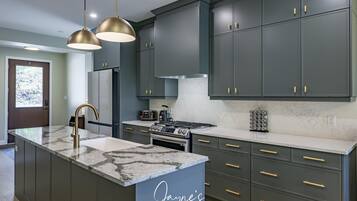 A modern kitchen with dark cabinets, gold handles, and a marble island.