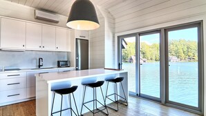A modern kitchen with white cabinets, a stainless steel refrigerator, a built-in oven, and a large island with bar stools. - AAA Lake Joe Prime Location Riverdale Rd! South! 8bdrm, 5 bath! Muskoka Beauty!! (Port Carling)