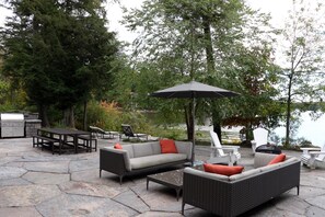 An outdoor patio with stone flooring, a grill, wicker furniture, and a view of a lake. - AAA Lake Joe Prime Location Riverdale Rd! South! 8bdrm, 5 bath! Muskoka Beauty!! (Port Carling)