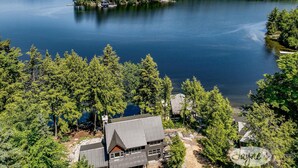 Un chalet au bord du lac, doté d’un toit en métal, entouré d’une forêt dense et de plusieurs petites îles.