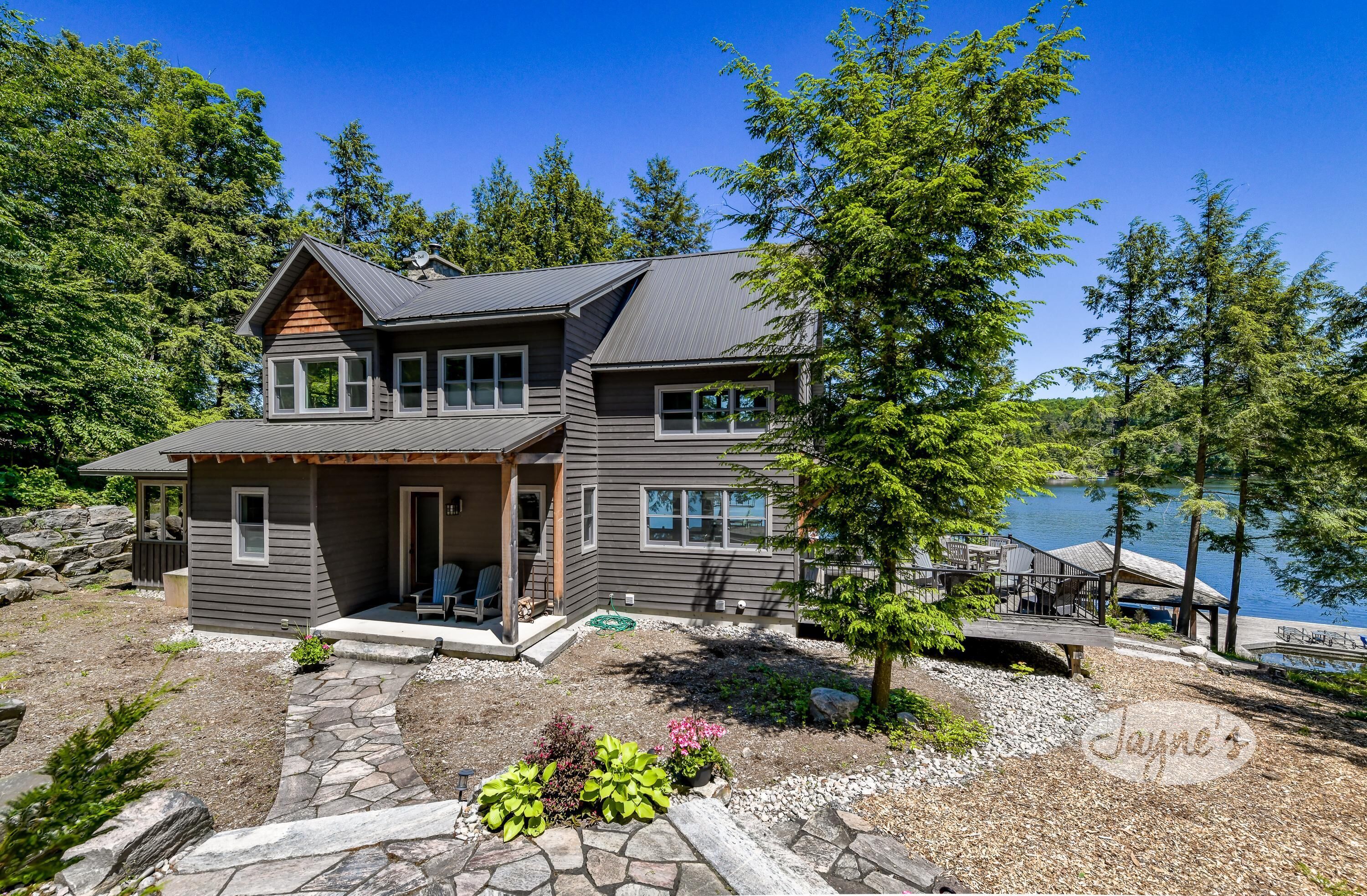 A two-story house with a dock extending into a lake, surrounded by trees.