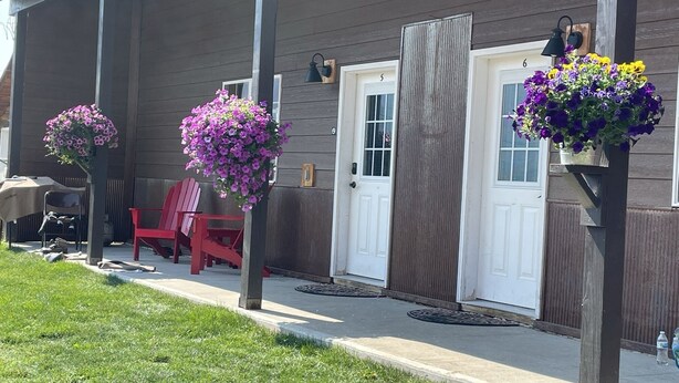 A building with a porch, red chairs, and hanging flower baskets. - The Antler Luxury Cabin! Cooke City, at the entrance of Yellowstone's NE Gate and Lamar Valley (Cooke City)