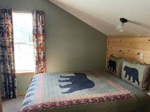 Une chambre à coucher avec un lit orné d’un motif en forme de puzzle, une fenêtre avec des rideaux à motifs et une tête de lit en bois.
