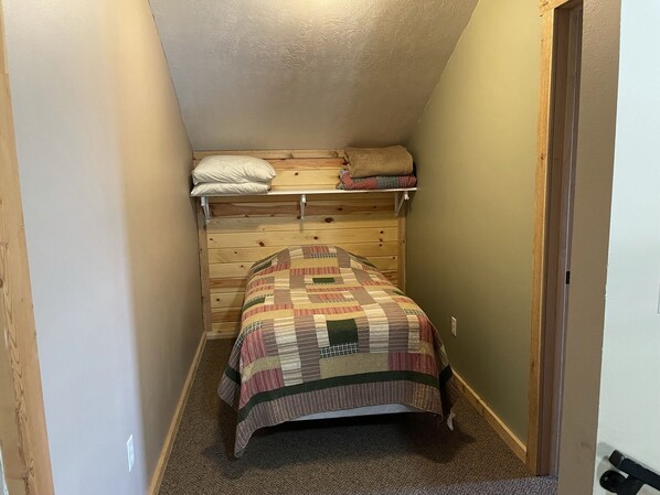 A small, narrow room with a bunk bed and a single bed, carpeted floor, and wooden walls.