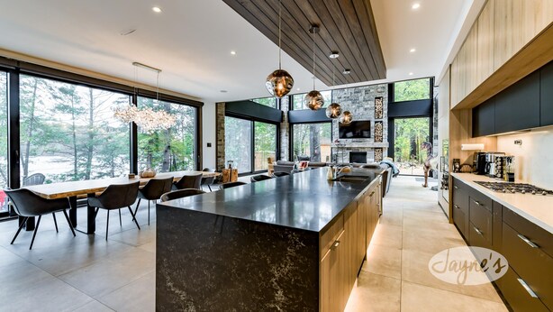 Une cuisine moderne dotée d’un grand îlot central, de meubles de rangement aux couleurs sombres et d’un pare-feu en pierre.