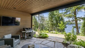 Une terrasse extérieure avec un sol en pierre, un barbecue et un téléviseur fixé au mur.