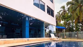 Um edifício moderno com piscina, espreguiçadeiras e palmeiras.