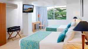 Habitación de hotel con dos camas, un escritorio, una silla, un televisor y ventana con vista a zonas verdes.