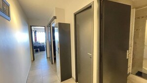 En hall med en dörr på höger sida, en dörr på vänster sida och en säng längre in i rummet.