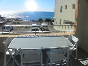 A balcony with a table and chairs, overlooking a parking area and the sea.