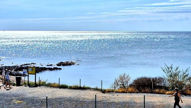 En kustvy med klar himmel, en sandstrand och en stenig kustlinje.