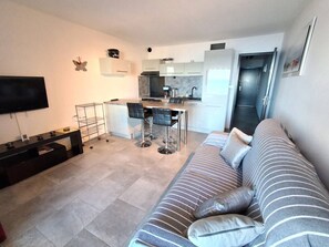 A modern living room with a sofa, a TV, a kitchen area with a dining table, and a kitchen island.