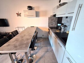A modern kitchen with a central island, white cabinetry, and a flat-screen TV mounted on the wall.