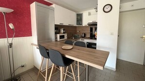 Een compacte keuken met witte kastjes, een houten aanrechtblad, en een zithoek met twee stoelen.