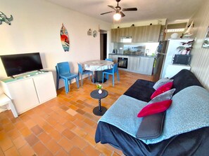 Um espaço de estar compacto com sofá, televisão, área de refeições, cozinha e ventoinha no teto.