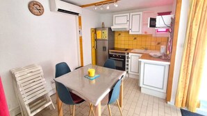 A compact kitchen with a dining table, chairs, a refrigerator, and a microwave. - APPARTEMENT EN REZ DE JARDIN POUR 4 PERSONNES (LE CAP D AGDE)