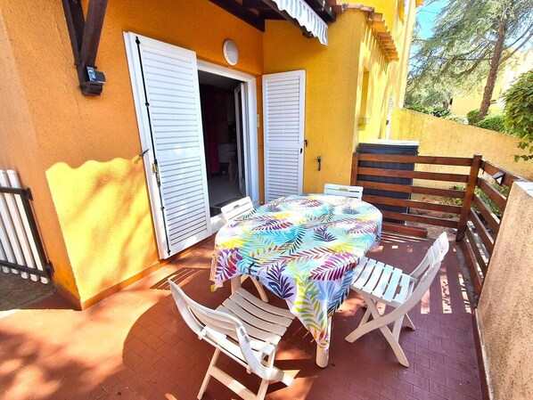 Um pátio externo com mesa e cadeiras, um banco de madeira e uma parede amarela.