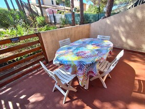 Pátio externo com mesa e cadeiras, cercado por um muro de madeira e vegetação.