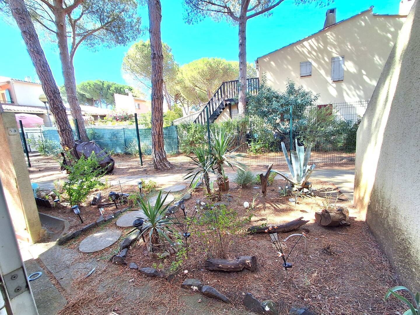 Un jardin avec des arbres, un chemin de pierres et une clôture.