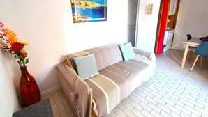 A living room with a sofa, a painting, a vase with flowers, and a dining area with a table and chairs. - APPARTEMENT EN REZ DE JARDIN POUR 4 PERSONNES (LE CAP D AGDE)