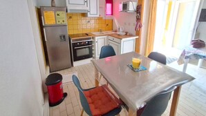 A compact kitchen with a refrigerator, oven, microwave, and a small dining area with a table and chairs. - APPARTEMENT EN REZ DE JARDIN POUR 4 PERSONNES (LE CAP D AGDE)