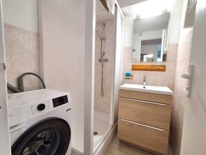 Uma casa de banho compacta com máquina de lavar roupa, chuveiro e lavatório com espelho.