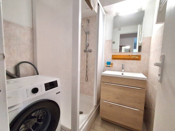 A compact bathroom with a washing machine, a shower, and a sink with a mirror.