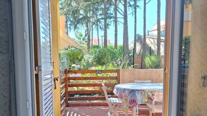 An outdoor patio with a table and chairs, a wooden fence, and a view of greenery and buildings. - APPARTEMENT EN REZ DE JARDIN POUR 4 PERSONNES (LE CAP D AGDE)