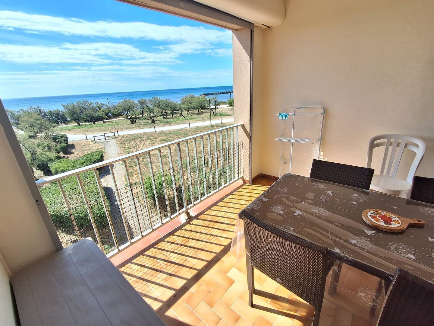 A balcony with a view of the sea, a table with chairs, and a drying rack.