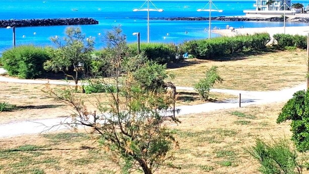 Blick auf die Küste mit blauem Himmel, einem Sandstrand und einem modernen Gebäude mit einem Balkon mit Meerblick.