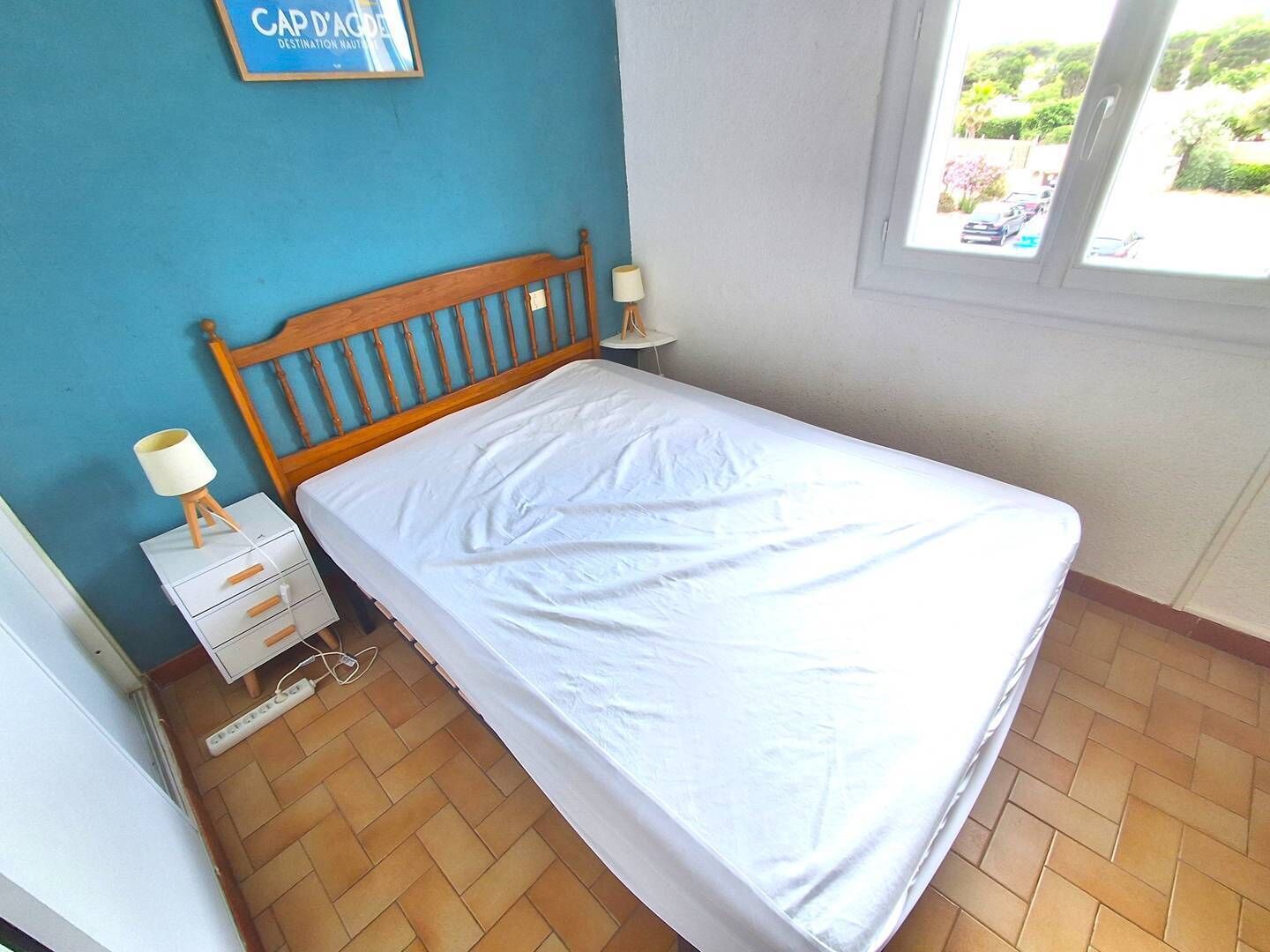 Une chambre à coucher avec une tête de lit en bois, un couvre-lit blanc, une table de chevet avec une lampe et une petite commode.